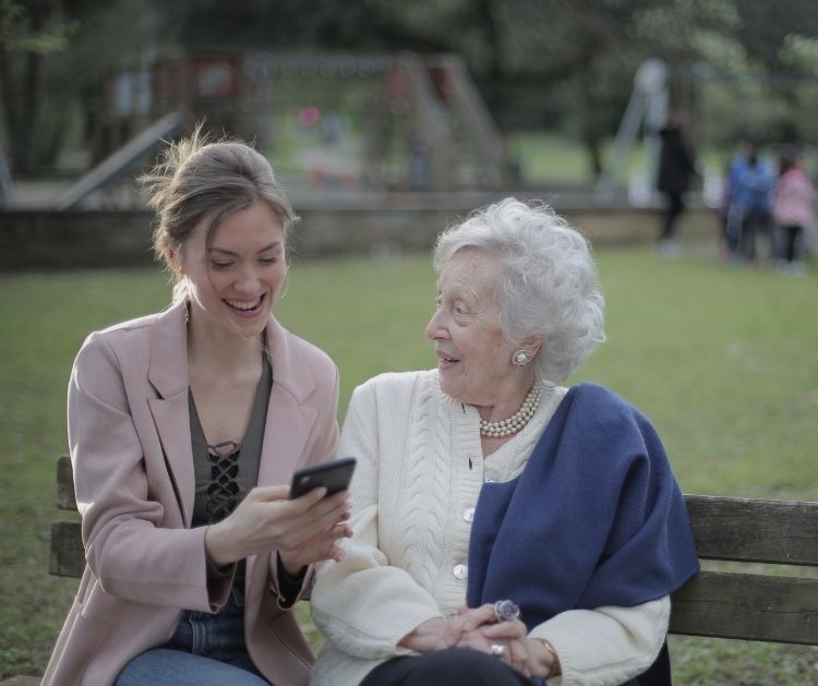 Young woman sitting next to older woman looking at her mobile. They're both smiling.